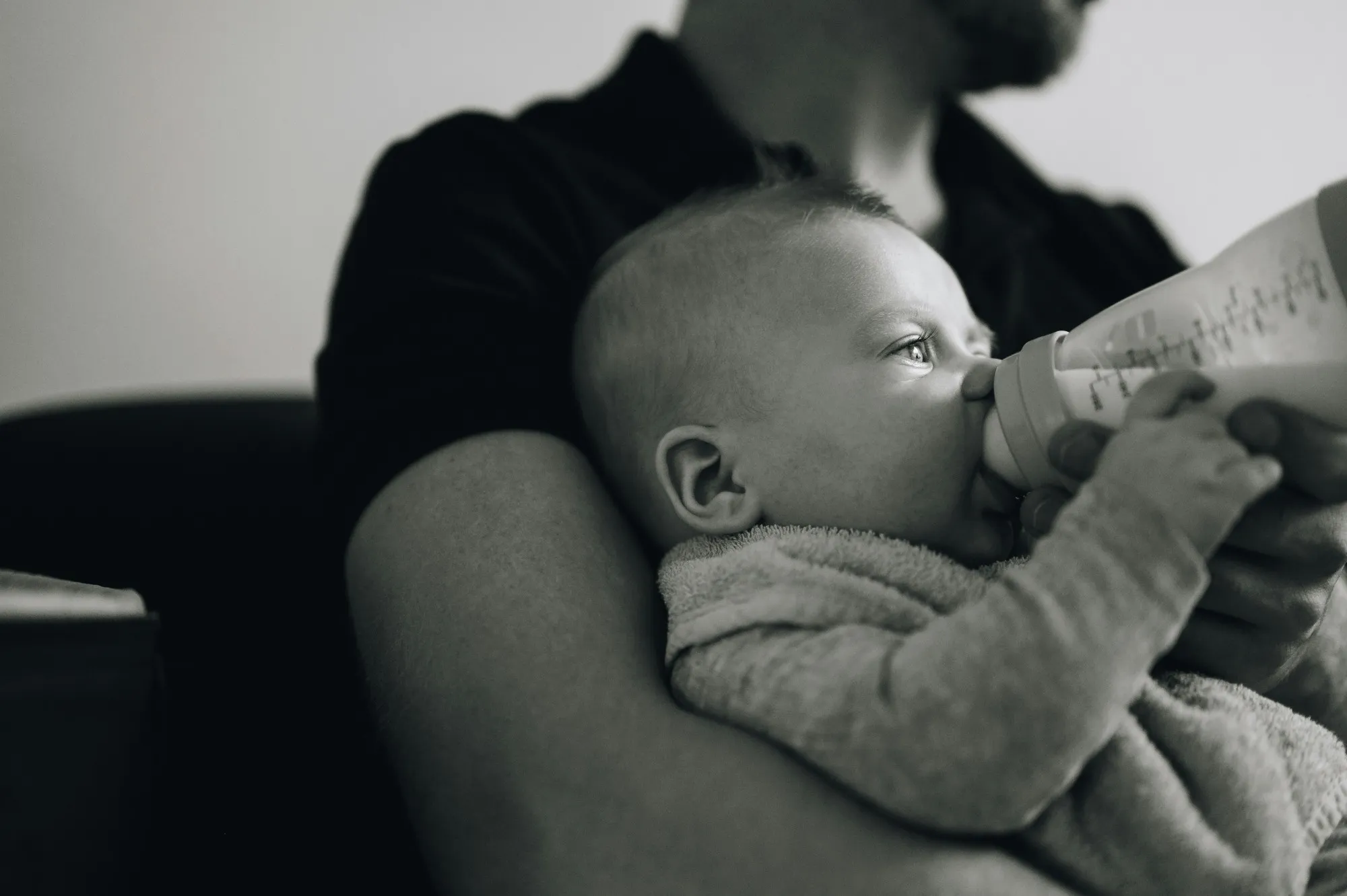 Dad holding his baby in the crook of his arm while the baby drinks from a bottle, in black and white