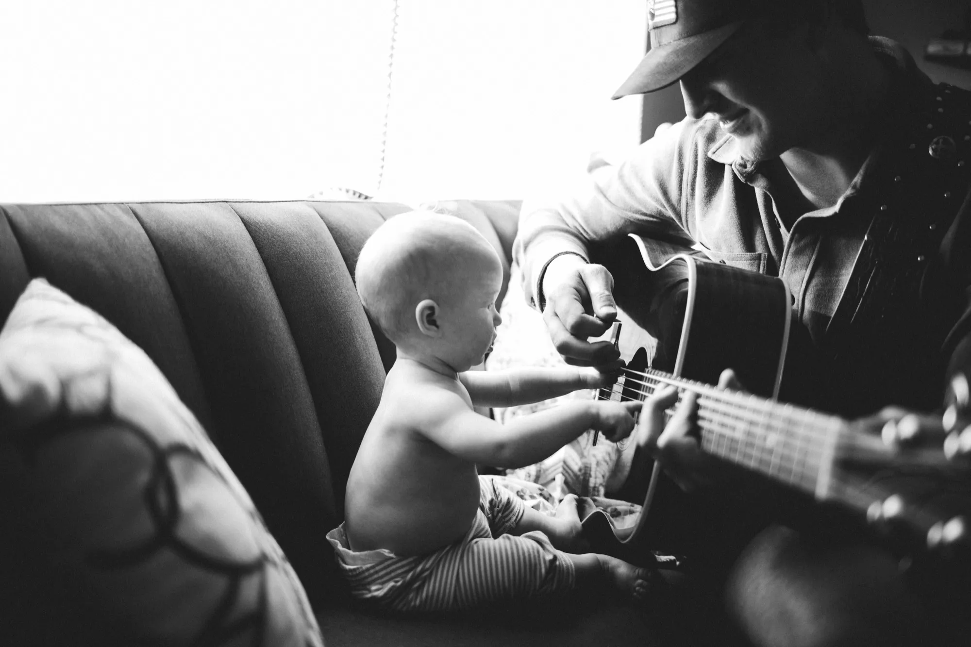 Baby on the couch reaching for the guitar while dad plays