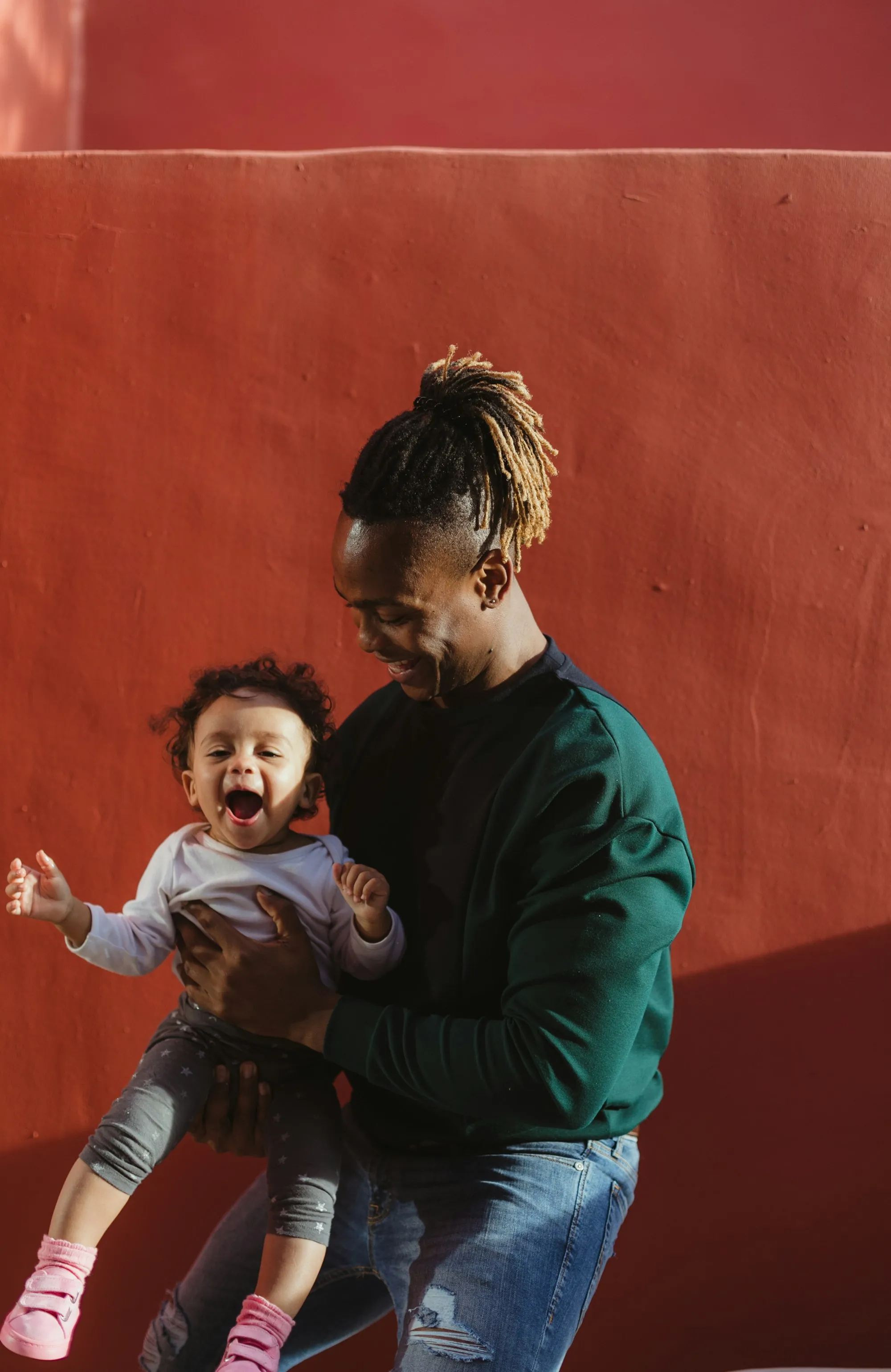 Dad holding his laughing toddler in front of a red wall