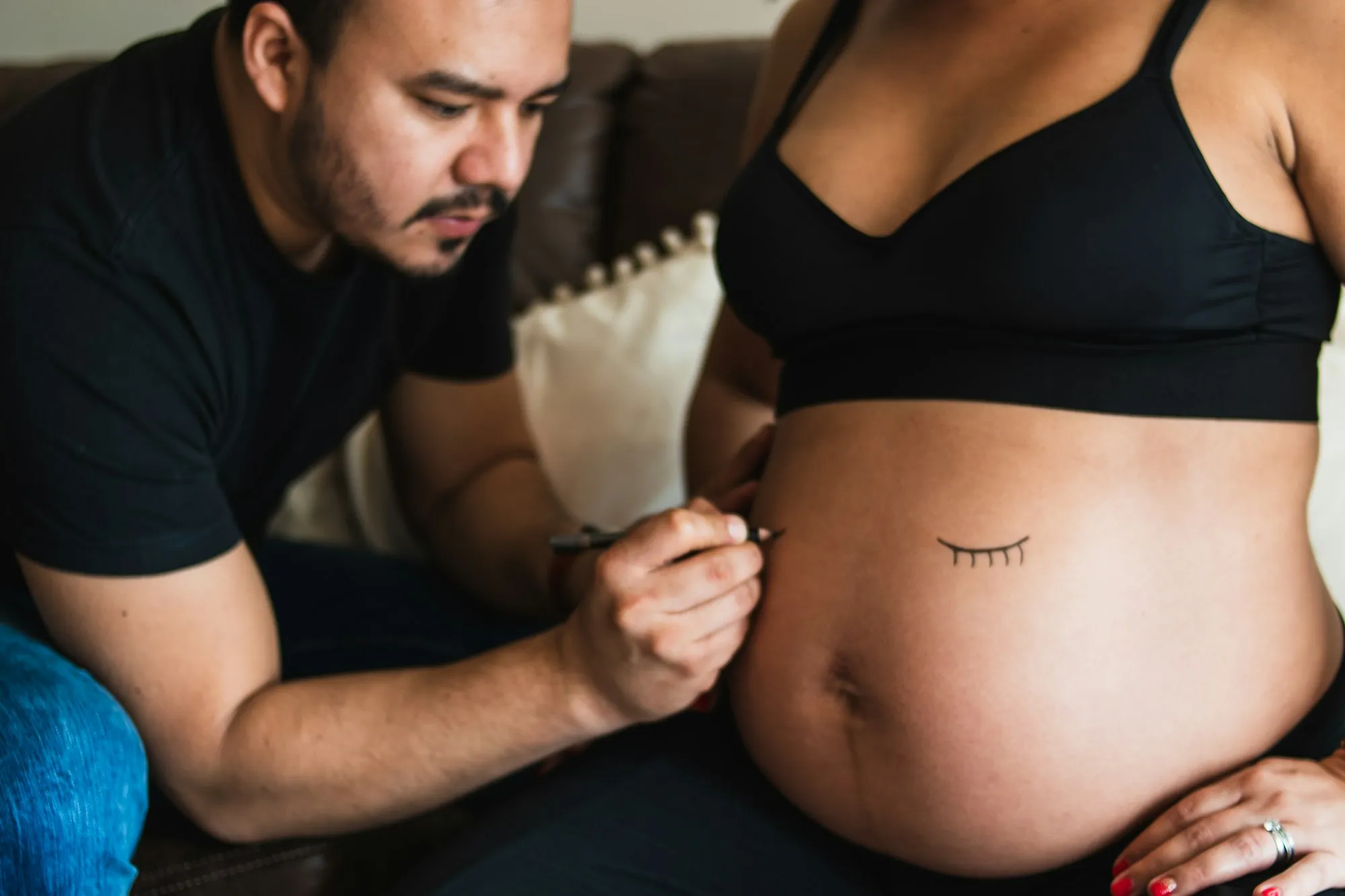 Man drawing a sleepy face on his pregnant partner's belly with a marker