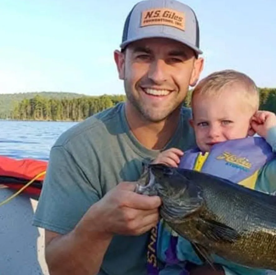 Smiling dad on a boat holding up a big fish next to his toddler in a life jacket
